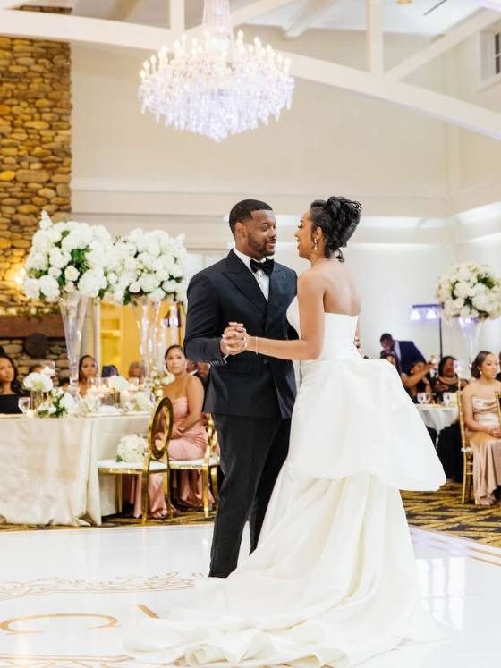 Couple first dance on a custom monogram dance floor wrap in a crystal-chandelier ballroom
