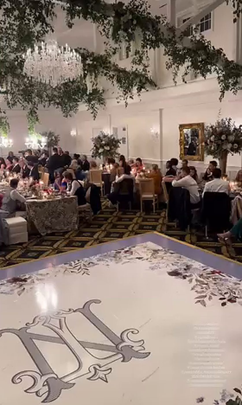 Large monogram dance floor wrap with a floral border in a ballroom with greenery and chandeliers