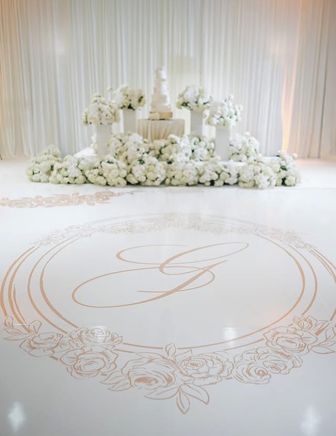 Gold script monogram in a rose wreath on a white dance floor wrap before a floral cake display at The Ritz-Carlton, Atlanta